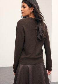 Brown sweater with a ribbed hem and textured back seam, paired with a brown leather skirt, featuring a smooth sheen.