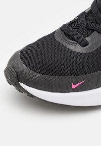 Scarpa sportiva nera con tomaia in mesh, tessuto testurizzato, swoosh Nike rosa e suola bianca. Presenta un laccio intricato e una punta arrotondata.