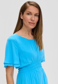 Lichtblauwe jurk met korte, gerimpelde mouwen en elastische taille. Gladde textuur, eenvoudige ronde halslijn, vloeiende silhouet.