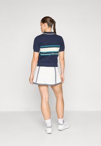 Polo de punto en color marino con mangas cortas que presenta franjas horizontales en tono teal y blanco, combinado con una falda corta blanca con ribete en color marino.