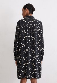 Czarna sukienka z długimi rękawami, zdobiona kremowym kwiatowym wzorem. Mankiety z guzikami, kołnierzyk oraz tylne zakładki zapewniające luźne dopasowanie.