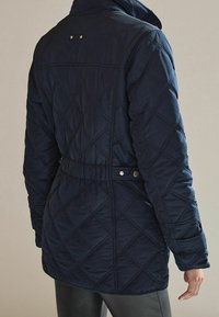 Giacca trapuntata blu navy con vita aderente, colletto alla coreana e bottoni automatici. Motivo a diamante testurizzato su tutto il tessuto.