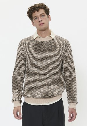 Knit sweater in beige with black and brown stripes, features a ribbed crew neckline and cuffs, layered over a light collared shirt.