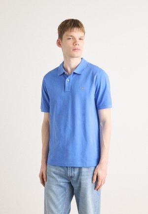 Polo en coton bleu avec des manches courtes, un col et un petit logo brodé sur la poitrine gauche. Porté avec un jean bleu clair.