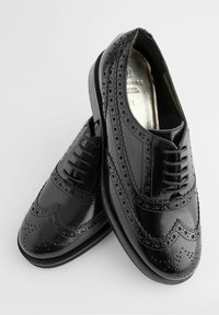 Zapatos de vestir de cuero negro con detalles de brogue, cierre con cordones y un acabado suave. Presentan una punta redonda y una suela texturizada.