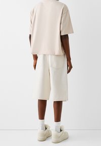 Valkoinen beige ylipitkä t-paita, valkoiset farkkushortsit, valkoiset sukat, beige tennarit. Yksinkertainen muotoilu, rento istuvuus, minimaalinen yksityiskohtaisuus.