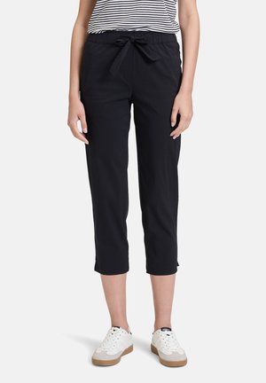 Pantalons capri noirs avec une taille élastique et une fermeture à lacets, dotés de poches latérales et d'une texture de tissu lisse. Associés à des baskets blanches.