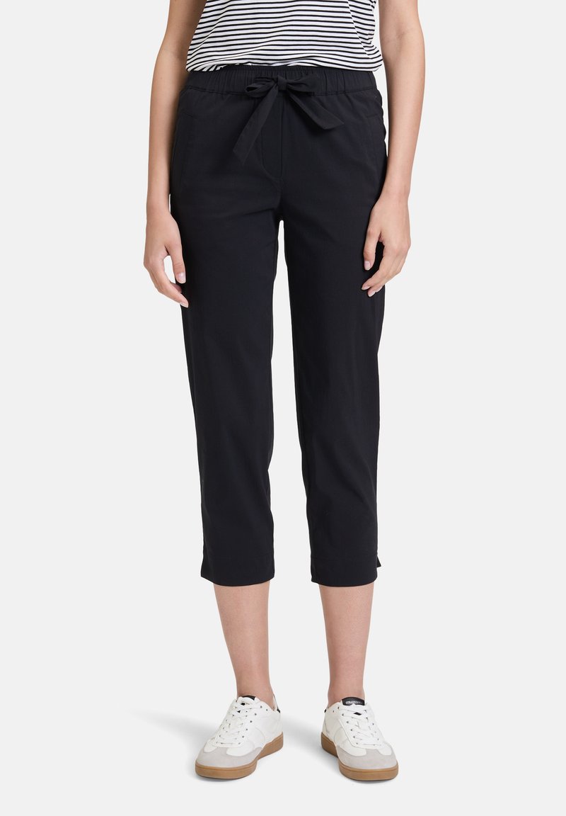 Pantalons capri noirs avec une taille élastique et une fermeture à lacets, dotés de poches latérales et d'une texture de tissu lisse. Associés à des baskets blanches.