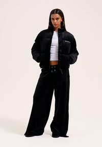 Casaco acolchoado preto com gola alta e fecho de correr, combinado com calças largas de veludo preto. Textura suave e design minimalista.