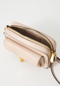 Lys beige skinn crossbody-veske med to glidelåsrom, hardware i gulltone, glatt tekstur og en frontklaff med lås.