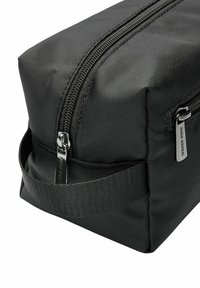 Zwarte rechthoekige tas van textiel, met een opvallende rits, zijhandvat en zilverkleurige hardware met merkdetails.