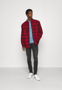 Red and black plaid flannel shirt over a light blue denim shirt, paired with black ripped jeans and white sneakers with red accents.