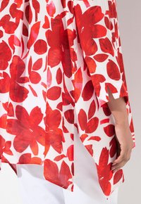 Blouse à motifs floraux rouges avec une coupe décontractée, en tissu léger, avec des manches trois-quarts et des fentes sur les côtés pour plus de liberté de mouvement.