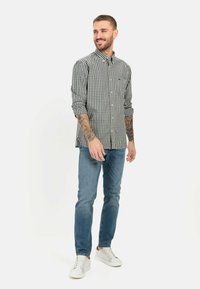 Herren Langarmhemd mit Karomuster in Schwarz und Weiß, aus Baumwolle, mit Knöpfen, mit hochgekrempelten Ärmeln. Kombiniert mit blauen Jeans und weißen Sneakers.