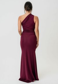 Burgundowa sukienka na jedno ramię wykonana z gładkiego, elastycznego materiału, z marszczeniami i dopasowanym krojem, który rozszerza się na dole.