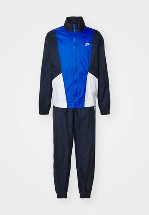 Chándal azul marino y blanco con una chaqueta con cremallera que presenta un gran panel azul. Hecho de un tejido suave y ligero, con puños elásticos.