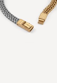 Bracciale in catena d'argento e oro con un design intrecciato. Caratterizzato da un clasp metallico inciso con il nome del marchio, offre colori e texture contrastanti.
