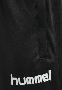 Czarne szorty sportowe wykonane z gładkiego materiału, z boczną kieszenią i białym logo w dolnym lewym rogu. Czysty, prosty design.