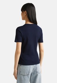 Námořnická modrá tričko s krátkým rukávem vyrobené z bavlny s kulatým výstřihem, s úzkým střihem a hladkou texturou. Nosené s světle modrými džíny.