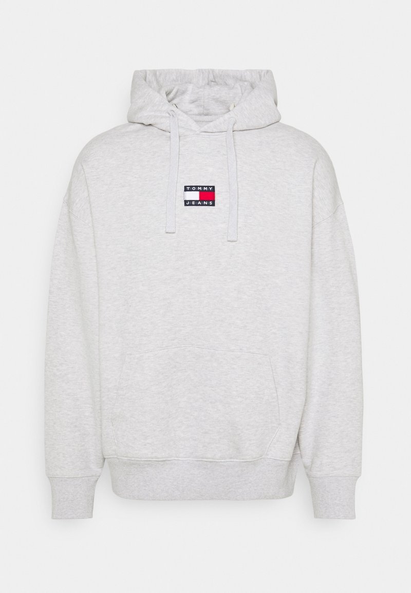 Felpa grigia chiara realizzata in misto cotone, con tasca frontale, cordini e un'etichetta logo rettangolare nei colori rosso, bianco e blu.
