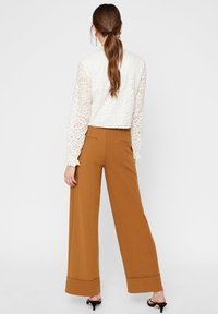 Haut en dentelle blanche à manches longues avec une coupe courte, associé à un pantalon marron à taille haute et jambes larges, doté de poches arrière et d'un ourlet à revers.