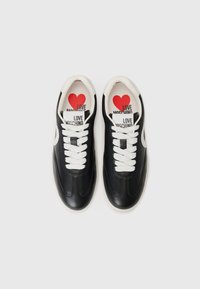 Juodi odiniai sportbačiai su baltais raišteliais ir padu. Viduje yra raudona širdies grafika su tekstu "LOVE MOSCHINO" ant vidpadžio.