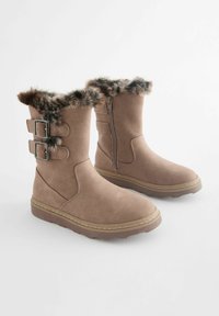 Botas de ante sintético marrón con un puño de pelo sintético, que cuentan con dos hebillas metálicas en el lateral y un cierre de cremallera. Suela de goma texturizada.