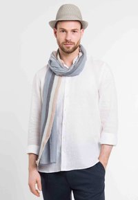 Könnyű, csíkos sál szürke, kék és beige színekben. Az élei rojtosak. Laza viselés egy fehér lening inggel és egy világos szalmakalappal.