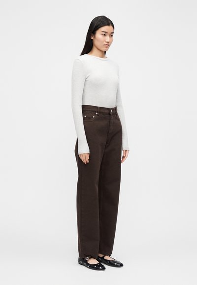 Barna, széles szárú nadrág magas derékkal, két elülső zsebbel és fém díszítésekkel, világosszürke hosszú ujjú felsővel és fekete balerinacipővel párosítva.