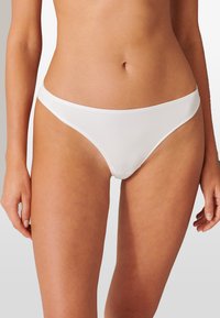 Bas de bikini blanc en tissu lisse, avec une coupe taille basse et des bandes latérales minimales. Design simple sans motifs ou accents visibles.