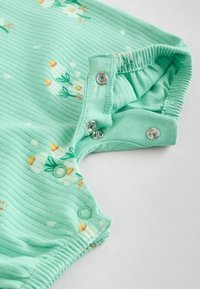 Lysegrøn ribbened jumpsuit med blomsterprint, udstyret med trykknapper ved skulderne og benåbningerne. Blød tekstur og elastisk kant.
