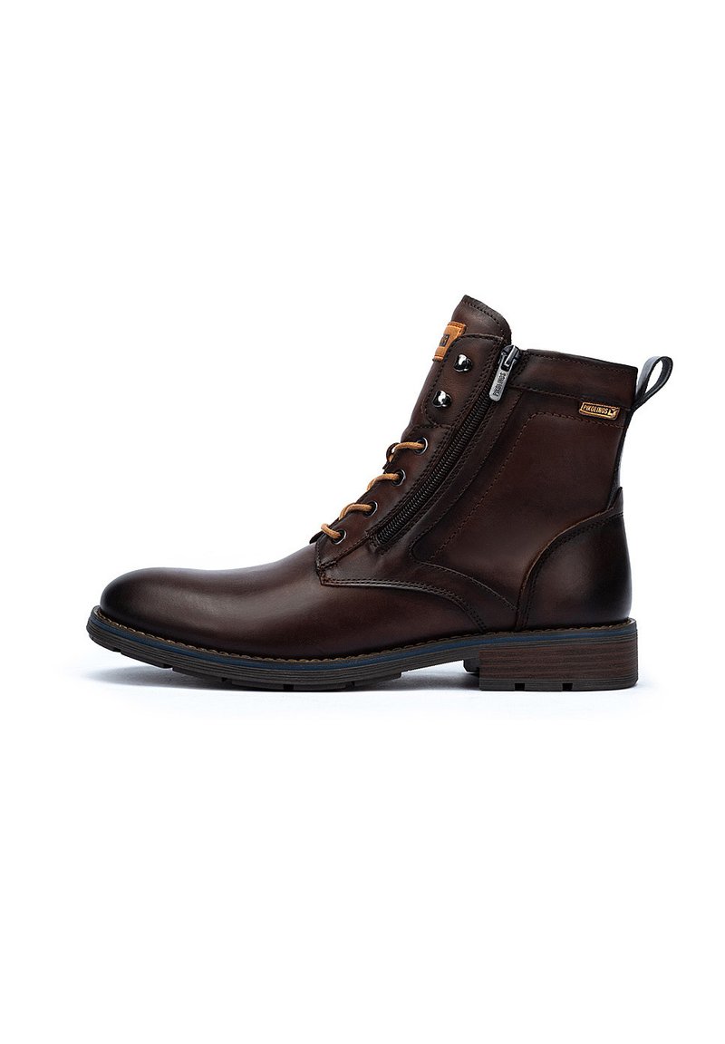 Bottines en cuir marron avec fermeture éclair sur le côté, œillets en métal et semelle texturée. Le design comprend une languette pour un enfilage facile.