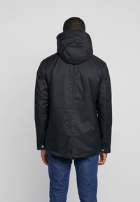 Sort, vandafvisende parka-jakke med aftagelig hætte, lange ærmer og snoretræk i kanten. Har en glat tekstur og knapdetaljer.