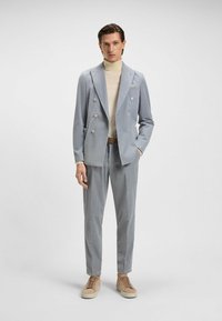 Lichtblauw gestreept pak met een dubbelzijdige colbert, bijpassende broek en een crèmekleurige coltrui; gecombineerd met beige suède sneakers.