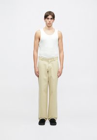 Hvit ermeløs tanktop, beige brede bukser og svarte sko. Stoffet ser glatt ut med en tettsittende design og en avslappet silhuett.