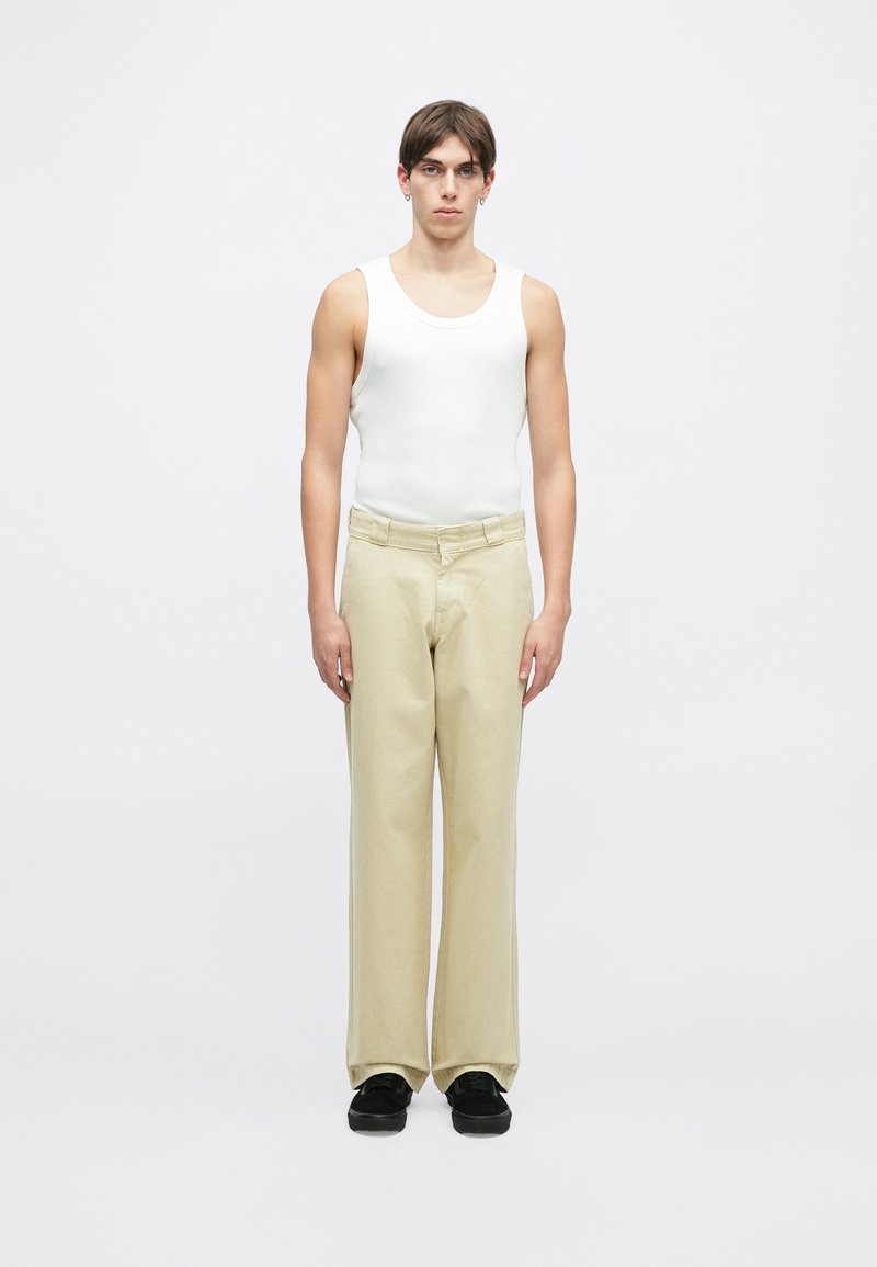 Hvit ermeløs tanktop, beige brede bukser og svarte sko. Stoffet ser glatt ut med en tettsittende design og en avslappet silhuett.