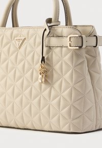 Beżowa pikowana torebka na ramię z trójkątnym logo, złotym wykończeniem i ozdobną zawieszką w kształcie klucza. Posiada przeszywany wzór diamentowy i regulowany pasek.