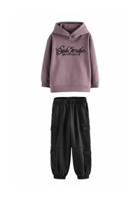 Haut à capuche violet clair avec des lettres noires et une grande capuche, associé à un pantalon cargo noir avec des poches latérales et des poignets élastiques.