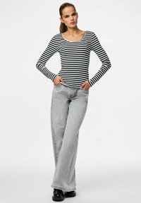 Černobílé pruhované tričko s dlouhým rukávem spárované se světle šedými rozšířenými džíny. Oblečení má dvě boční kapsy a volný střih.