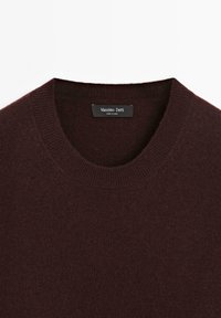 Maglione a maglia bordeaux con scollatura rotonda, texture liscia e un'etichetta con la dicitura "Massimo Dutti". Design classico adatto per essere indossato a strati.