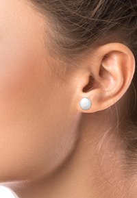 Boucle d'oreille en argent avec une surface lisse et ronde et une finition polie, portée sur le lobe de l'oreille. Le ton de peau est neutre.