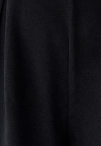 Črna tkanina z gladko teksturo. Material je mehak in mat, z rahlim sijajem pod določenimi svetlobnimi pogoji. Značilne so čiste, ravne linije.