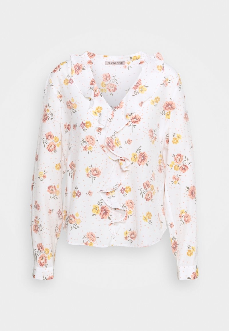 Blouse blanche à fleurs avec des fleurs roses et jaunes, des volants le long de l'encolure et des manches longues. Tissu doux avec une texture légère.