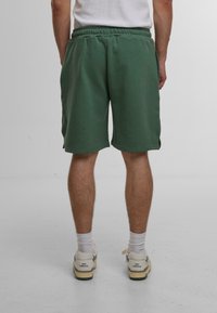 Shorts en coton verts avec une taille élastique, des poches latérales et une coupe décontractée, associés à des chaussettes de sport blanches et des baskets.