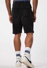 Pantalones cortos de mezclilla negra con dobladillos enrollados, cinturilla elástica y dos bolsillos traseros. Combinados con zapatillas blancas de caña alta y calcetines con patrones.
