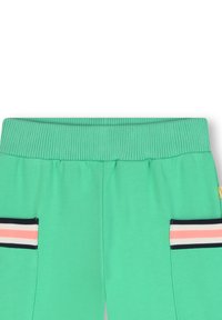 Groene sweatpants hebben een geribde tailleband, zijzakken met zwart en roze gestreepte accenten, en een gladde textuur.