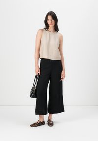 Beige top bez rukávů, černé kalhoty s širokými nohavicemi a baleríny se zvířecím potiskem. Modelka drží malou černou kabelku. Hladká tkanina, volný střih a strukturovaný design.