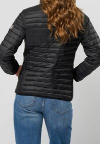 Černá prošívaná bunda s horizontálním prošitím, s logem na levém rukávu, kombinovaná s modrými džíny.