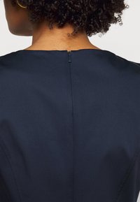 Robe bleu marine avec une texture lisse, dotée d'une fermeture éclair au dos et d'un design minimaliste. Lignes épurées et détails de couture subtils.