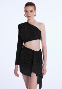 Černý třpytivý top s jedním dlouhým rukávem a řasenou mini sukní s asymetrickým designem a bočním záhybem.